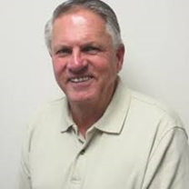 A man with grey hair and white shirt smiling.